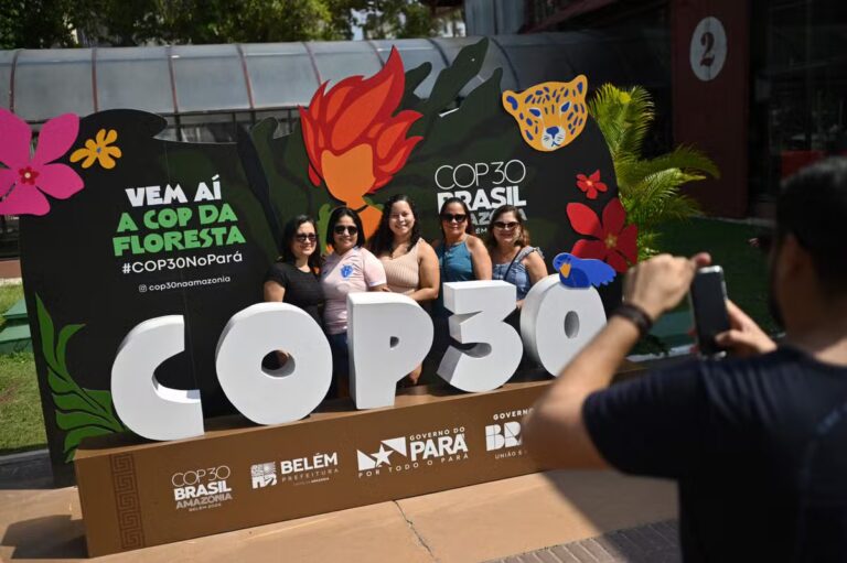 112970345-people-pose-for-a-picture-with-a-banner-of-the-cop30-inside-the-estacao-das-docas-a-touris.avif