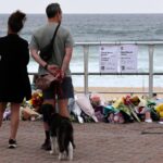 113319319-a-couple-pauses-at-floral-tributes-on-bondi-beach-to-pay-respects-to-the-victims-of-the-sy.jpeg