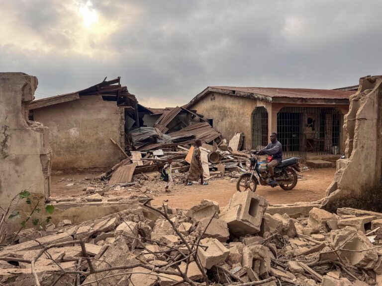 113389374-topshot-residents-and-a-motorcyclist-move-between-destroyed-structures-in-offa-on-decemb.j.jpeg
