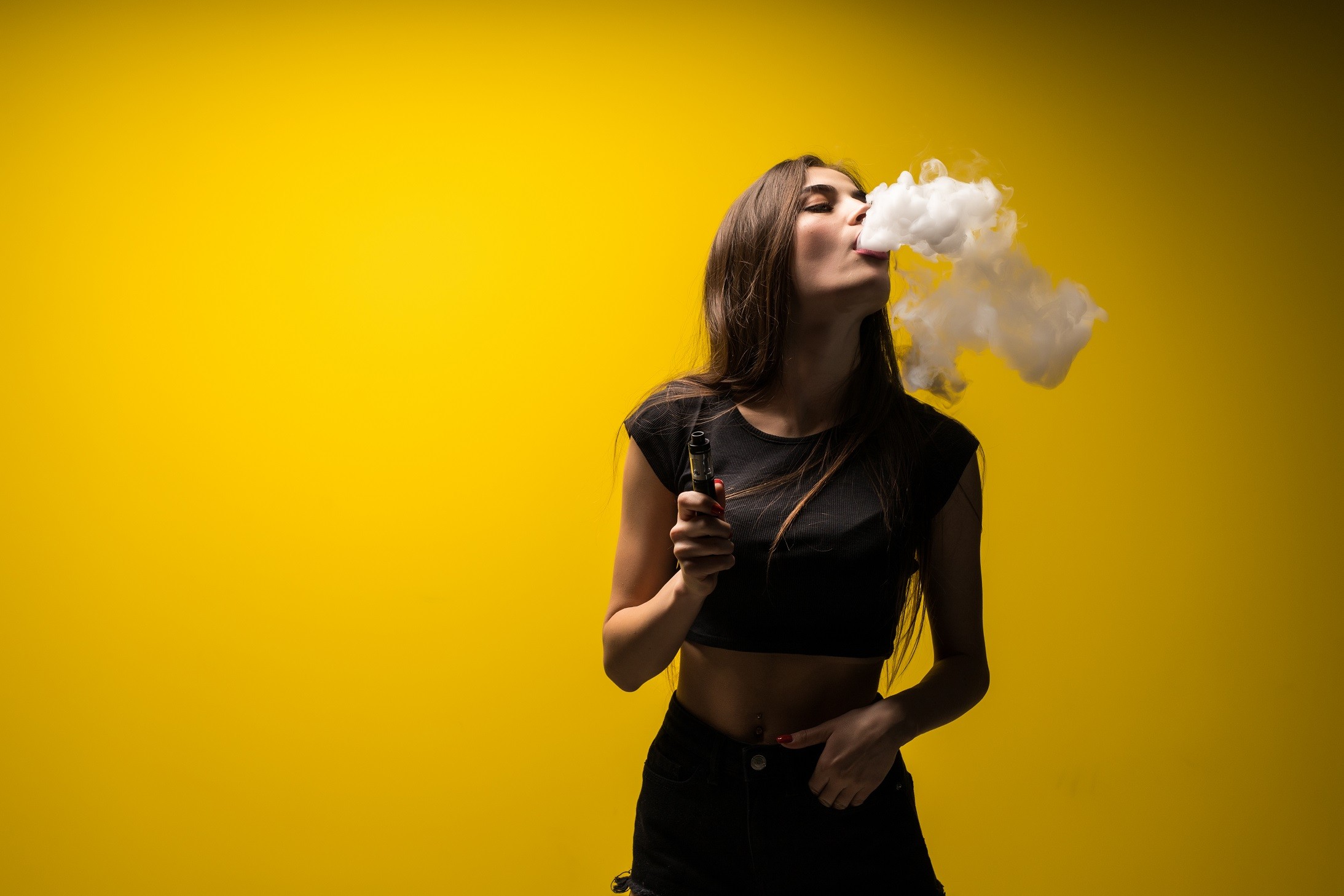 attractive-woman-standing-vaping-yellow-wall.jpg