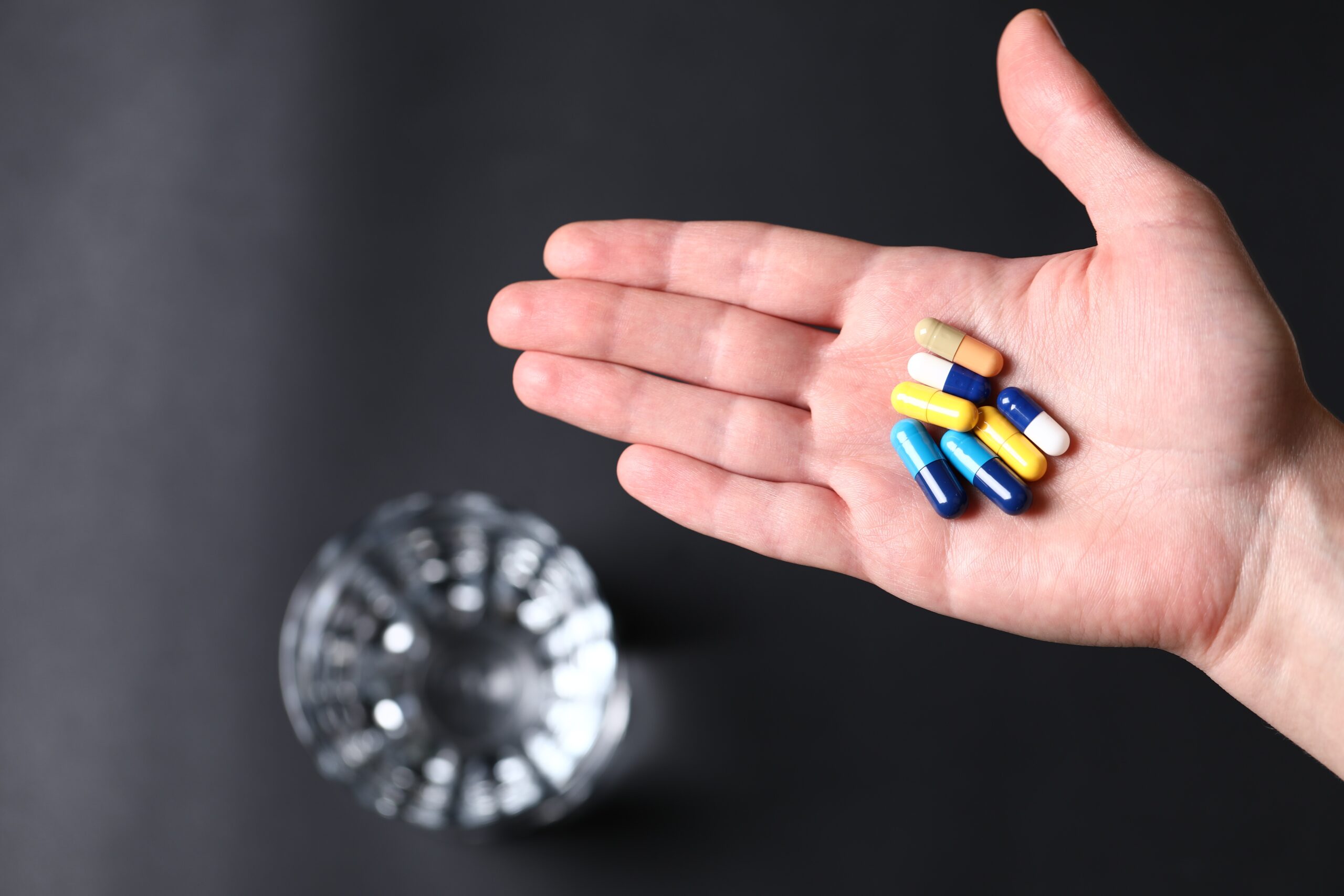 colorful-medical-pills-hand-person-glass-water.jpg